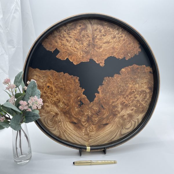Round burr elm and black resin ottoman tray displayed upright with flowers in foreground