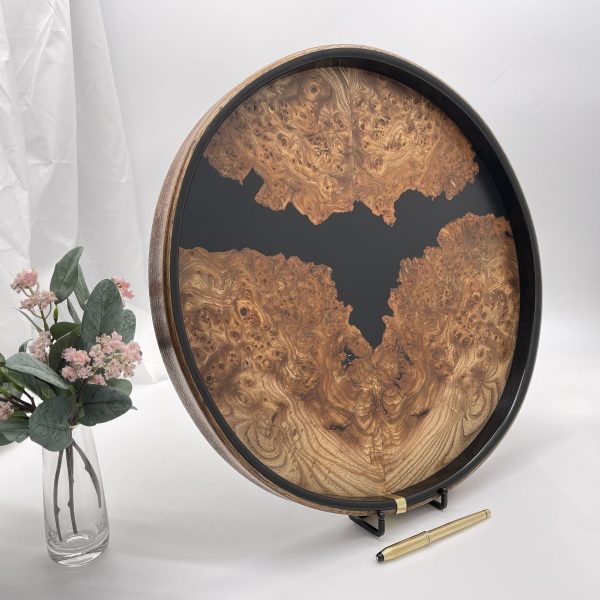 Round burr elm and black resin ottoman tray displayed upright with flowers in foreground